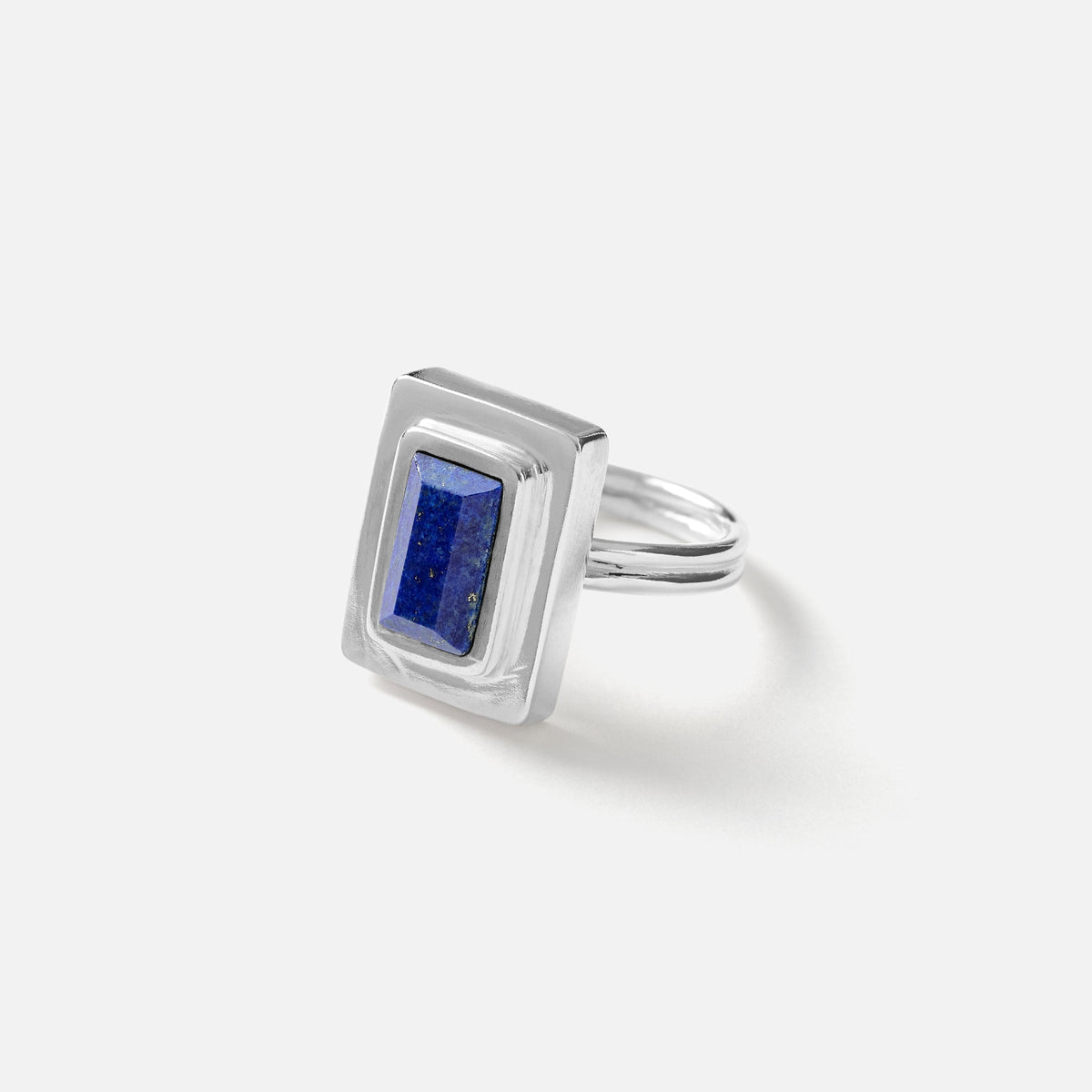 A silver ring featuring a rectangular bezel-set lapis lazuli stone, photographed on a clean, light gray background.