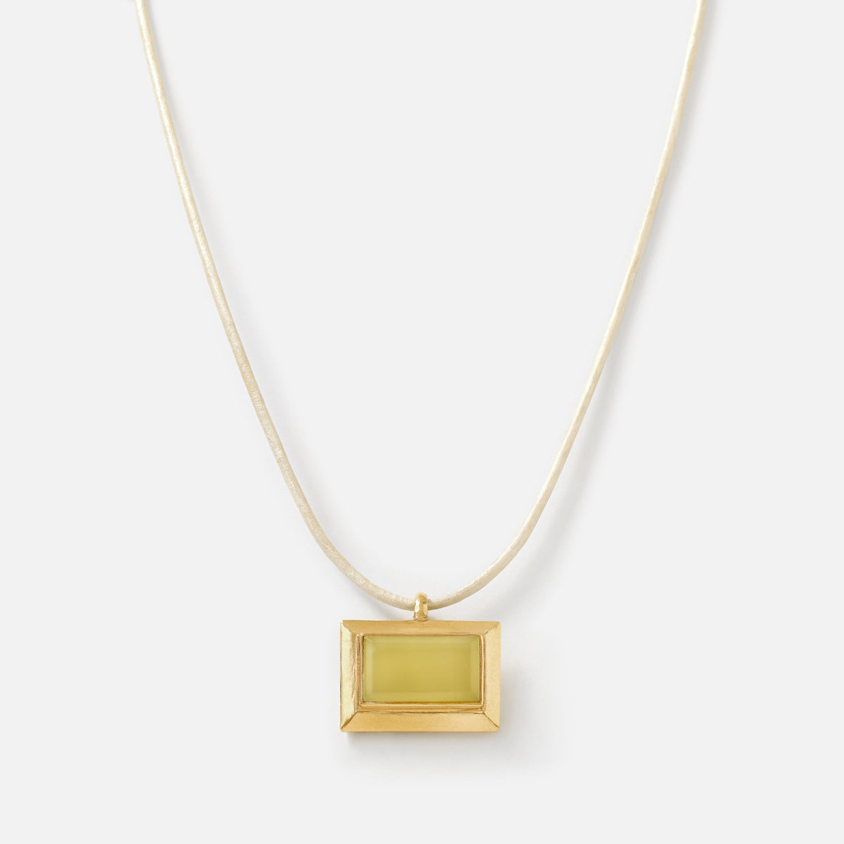 A gold necklace with a rectangular pendant featuring a pale yellow-green center, suspended from a delicate gold chain against a light gray background.