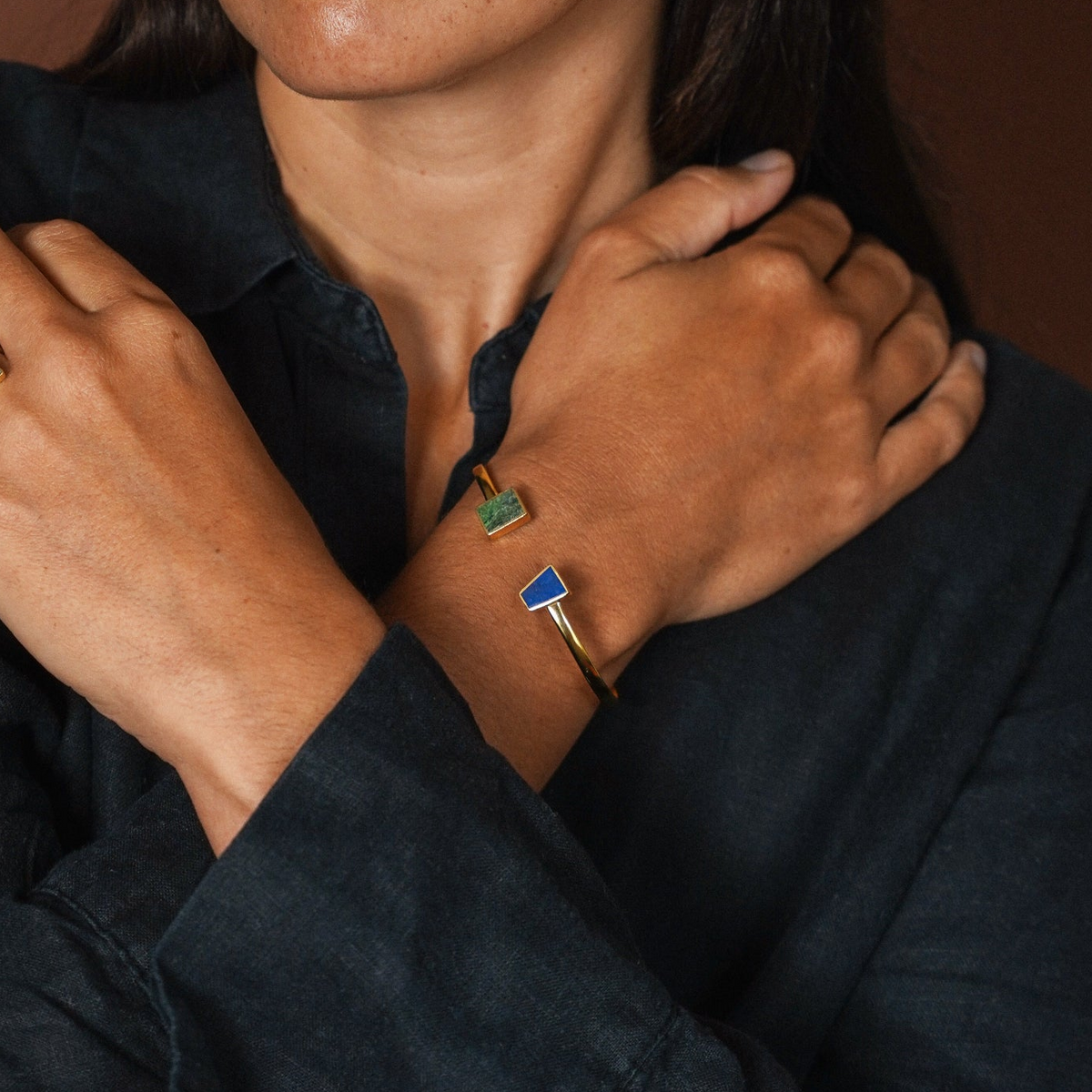 Woman's wrist with gold bangle with stones of lapis and crysocolla. Brown background.