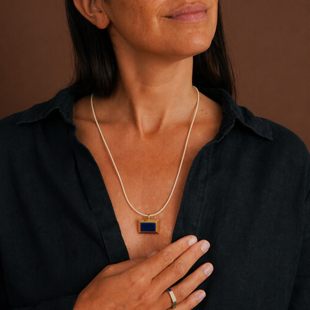 woman wearing pendant on a long cord, wearing a dark shit on a brown background