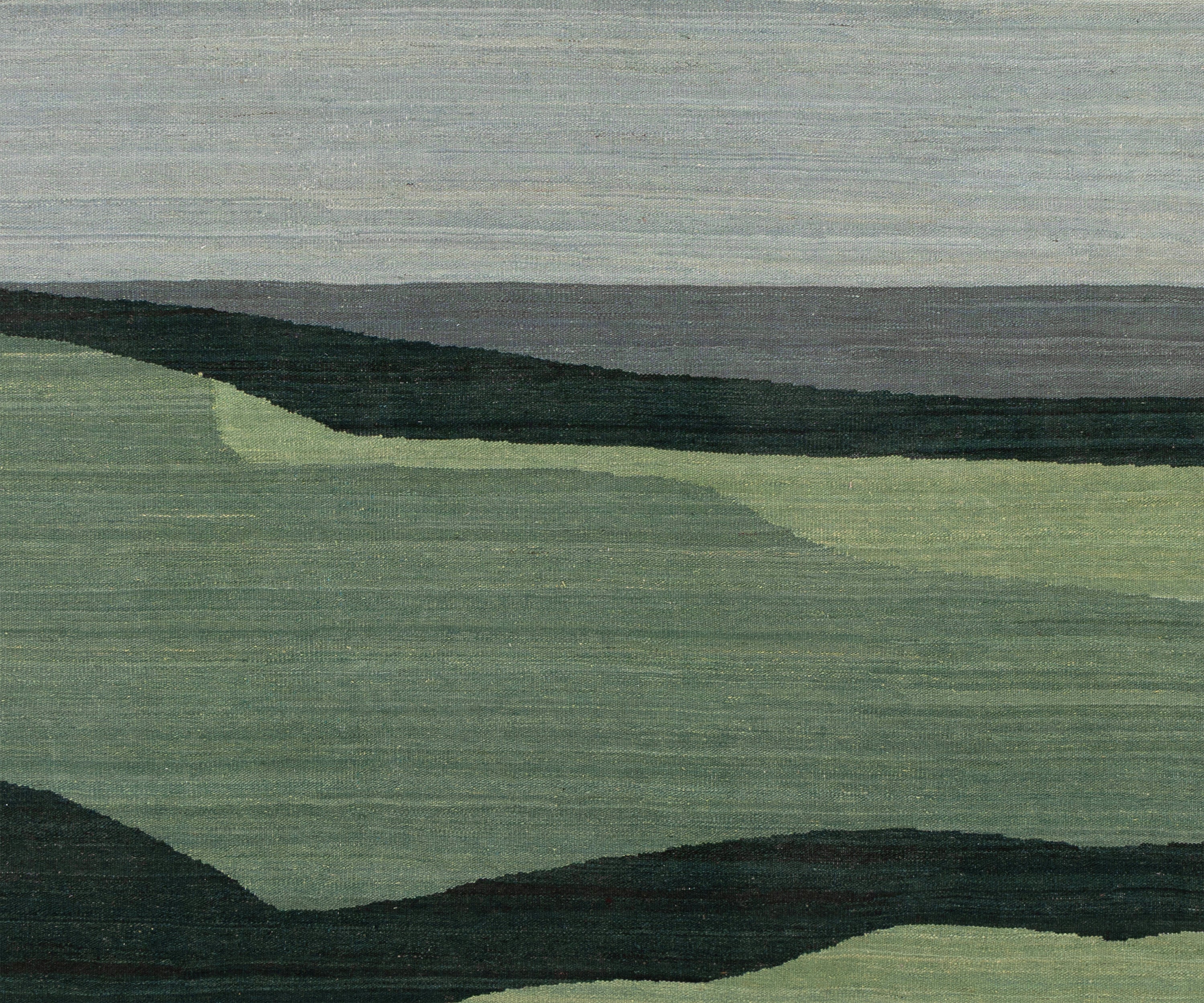 A close-up of a woven rug or textile featuring a minimalist landscape design with layered green hills, dark charcoal landforms, and a muted gray sky.