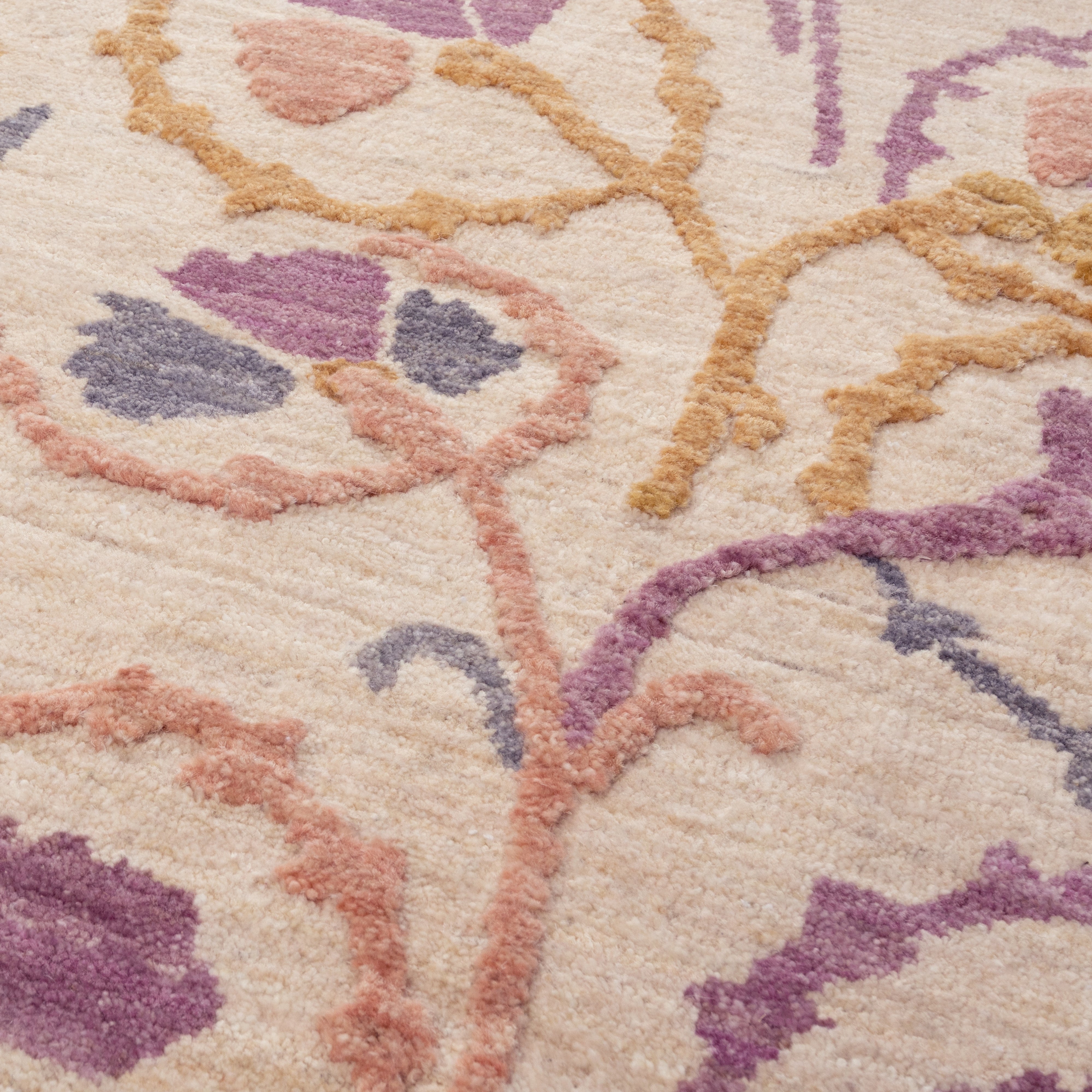 Close-up of a hand-knotted textured wool rug with floral patterns in purple, pink, and beige.