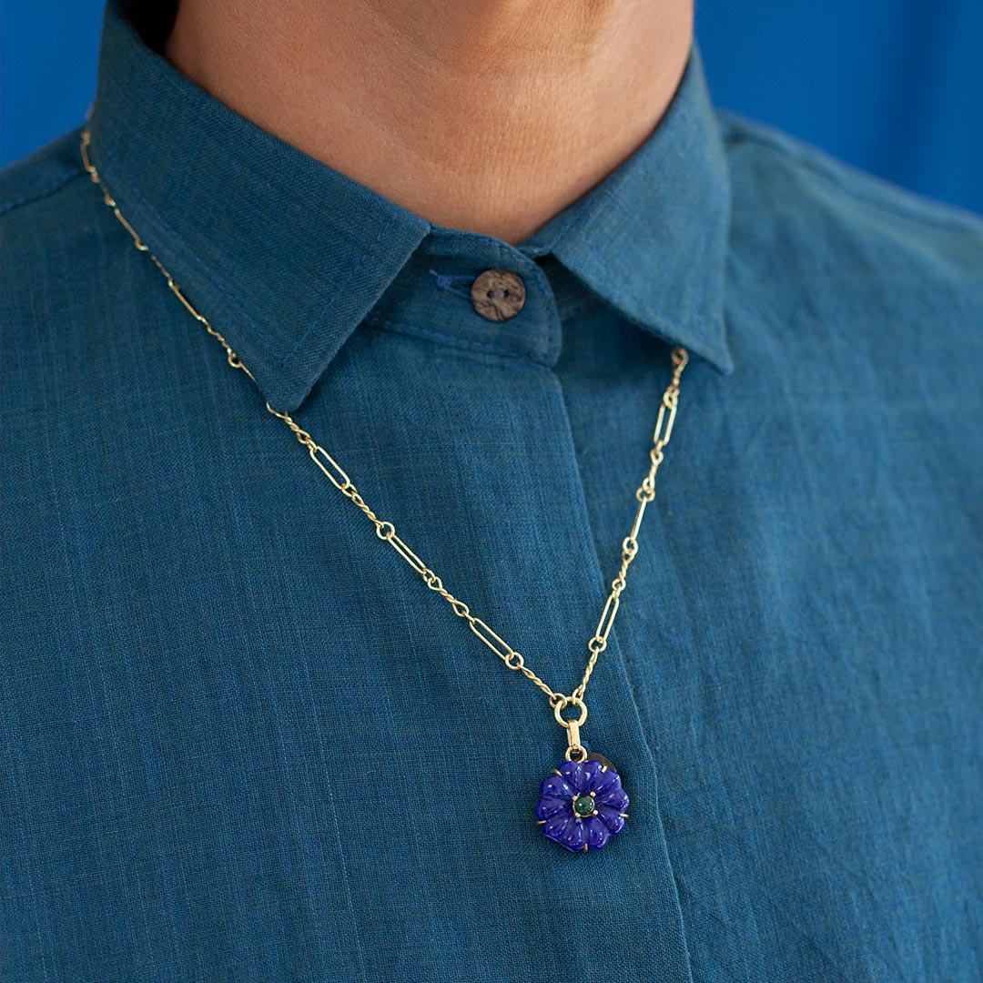 Gold-plated necklace with a lapis pendant on a person wearing a blue shirt against a blue background