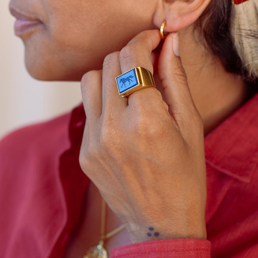 Person wearing a gold-plated ring with a carved horse on blue Agate stone.