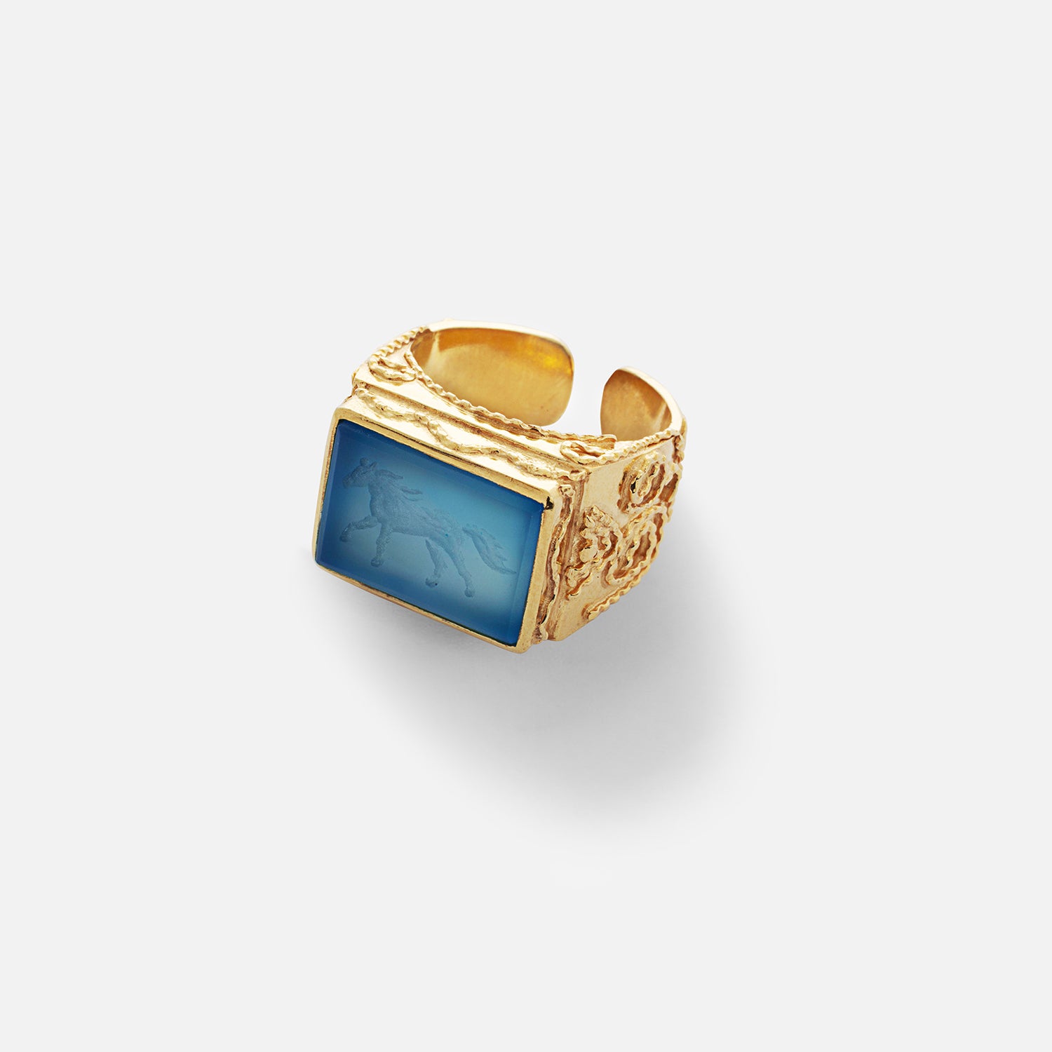 A gold-plated filigree ring with a blue agate stone depicting a silhouette of a galloping horse.