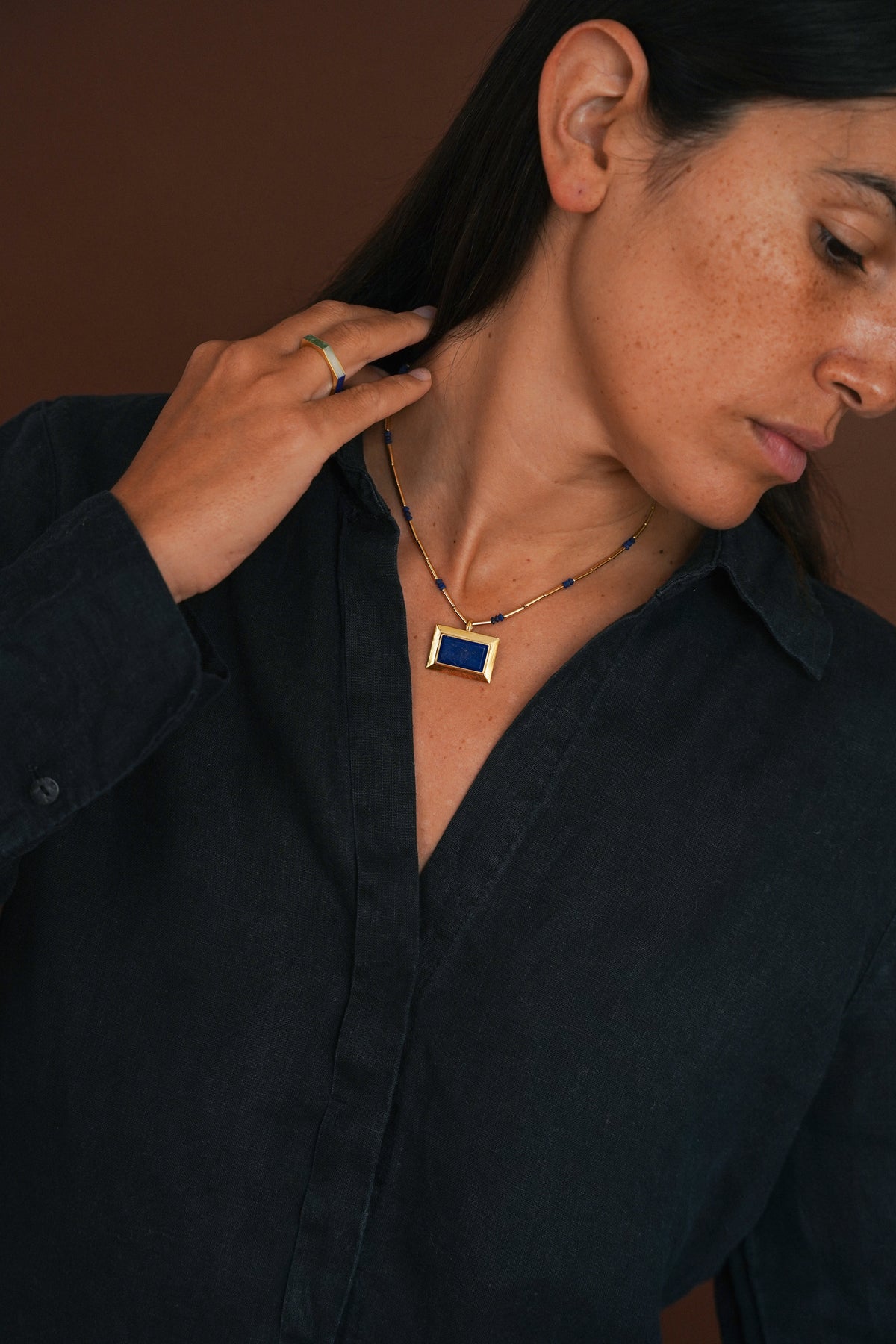 women wearing rectangular gold-plated pendant with lapis stone, on a beaded choker chain, with brown background.