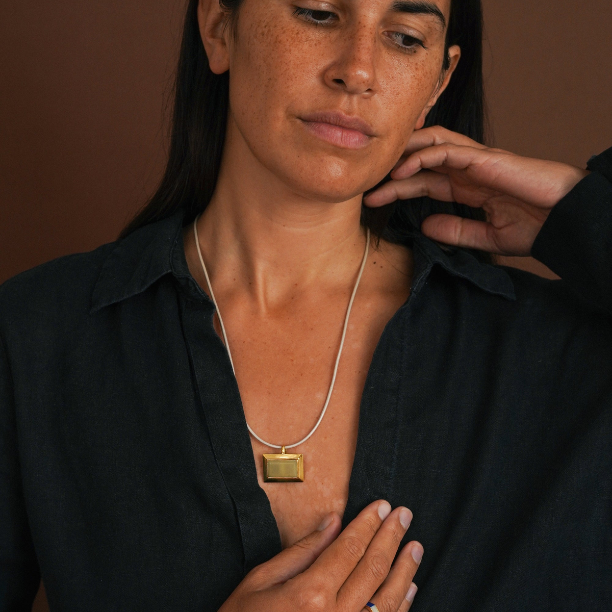 woman with dark hair wearing pendant on leather cord and a dark shirt. Brown background