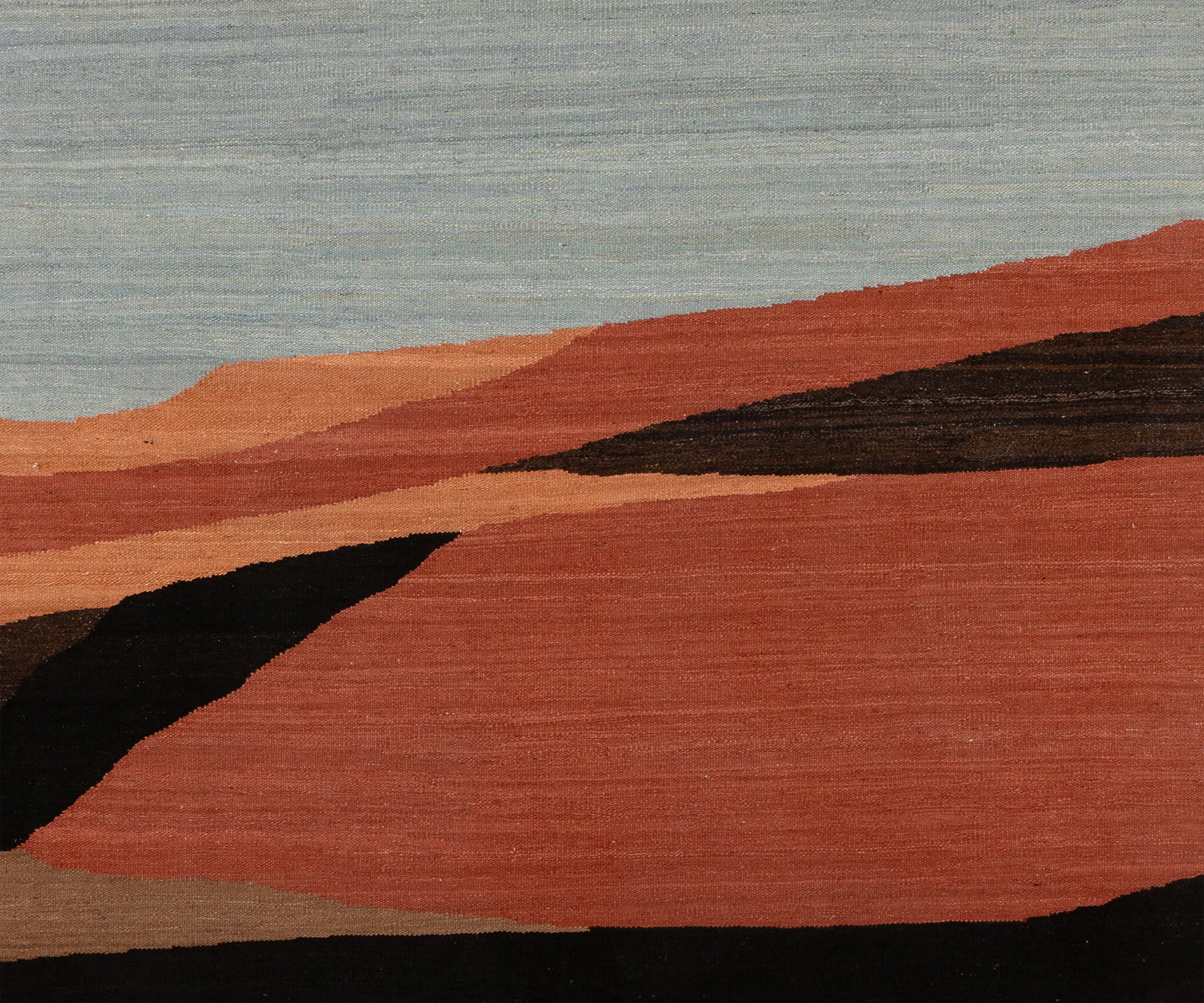 Abstract landscape-style textile or rug with layered geometric hills in terracotta, rust, peach, black, and taupe beneath a pale blue-gray sky.