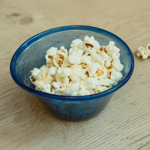 Blue hand-blown glass bowl filled with popcorn on a wooden surface