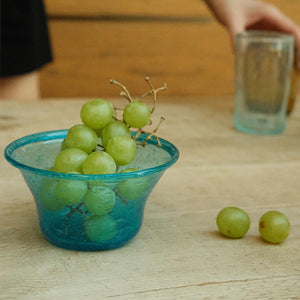 Green grapes in a turquoise hand-blown glass bowl on a wooden surface