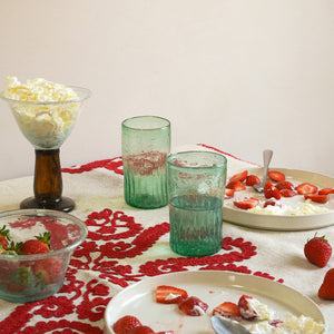 Table setting with handblown ripple green glasses, strawberries and cream on a red lace tablecloth