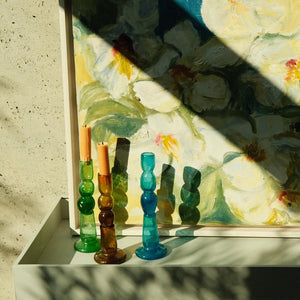 Colorful glass candle holders on a table with a floral painting in the background