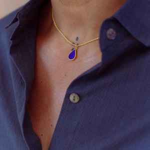 Person wearing a gold plated sterling silver necklace with a teardrop-shaped blue Lapis Lazuli pendant.