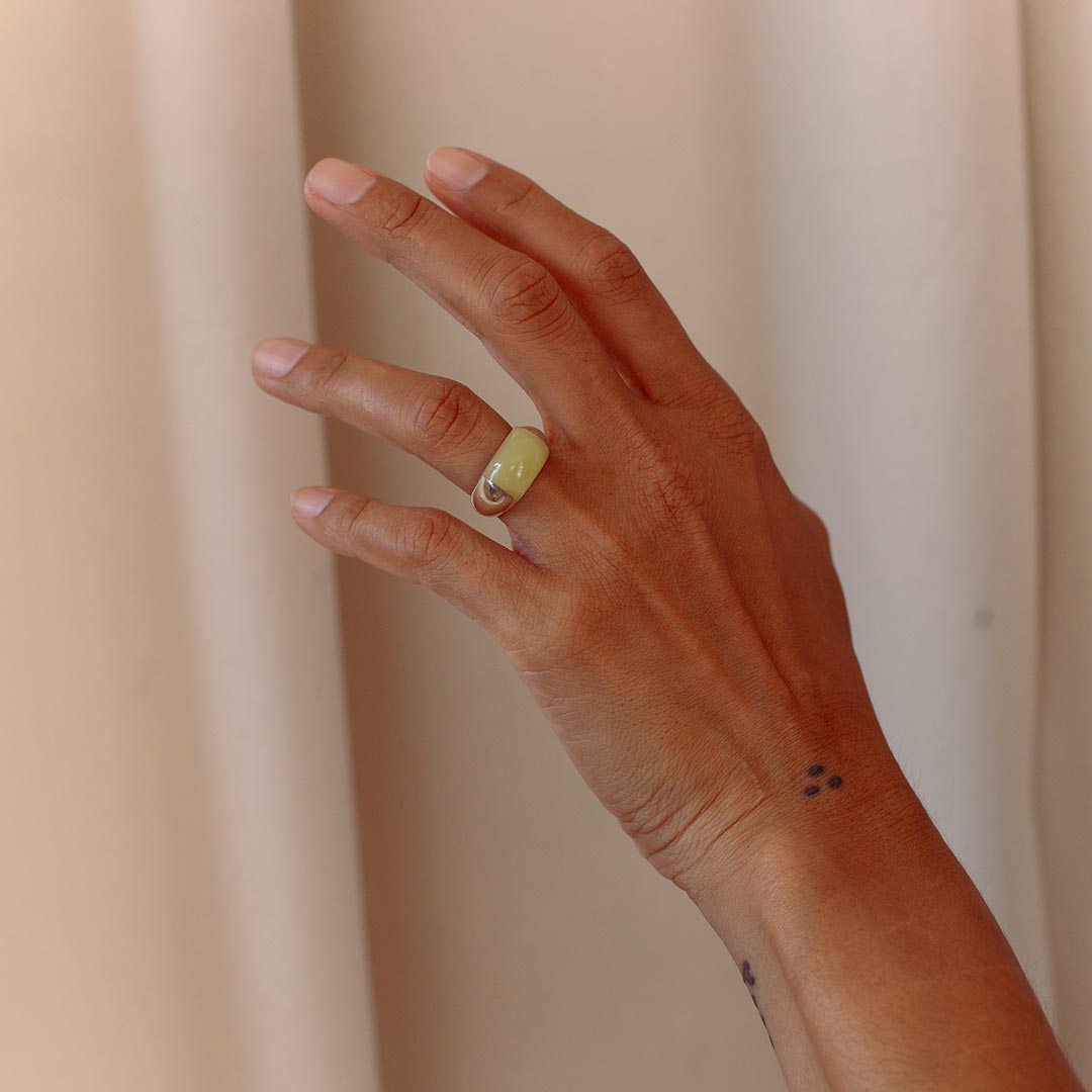 Hand with sterling silver chunky ring with green onyx stone against beige background