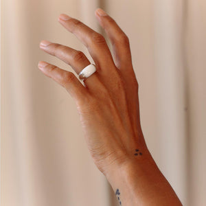 Hand wearing a sterling silver chunky ring with white marble on a plain background