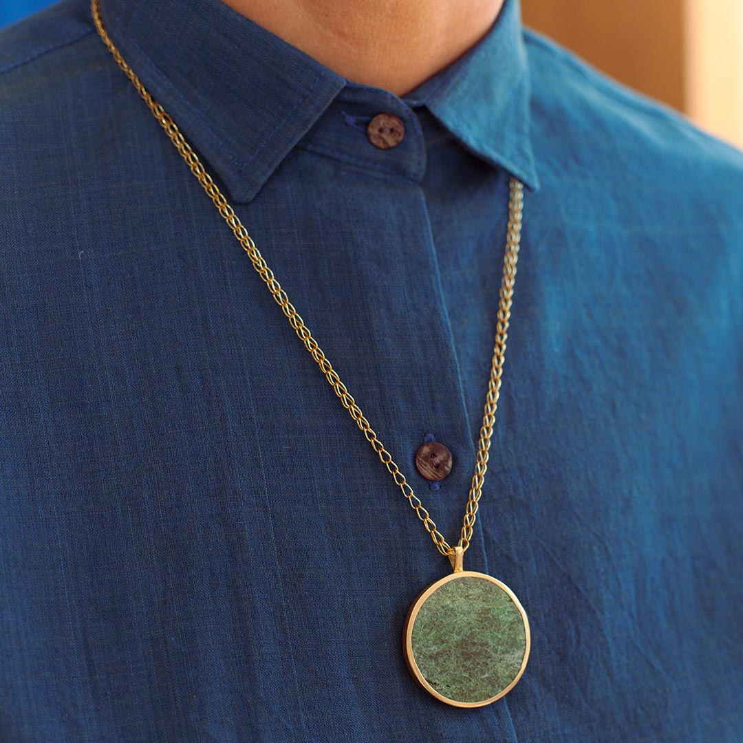 Person wearing a blue shirt with a gold chain ISHKAR pendant.