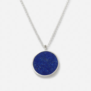 A pendant necklace with a large circular disc featuring a blue stone, Lapis Lazuli, set in a silver frame, attached to a silver chain.