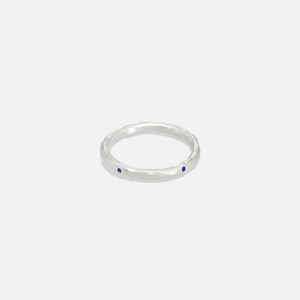 A simple silver band ring with two small blue stones on the top surface.
