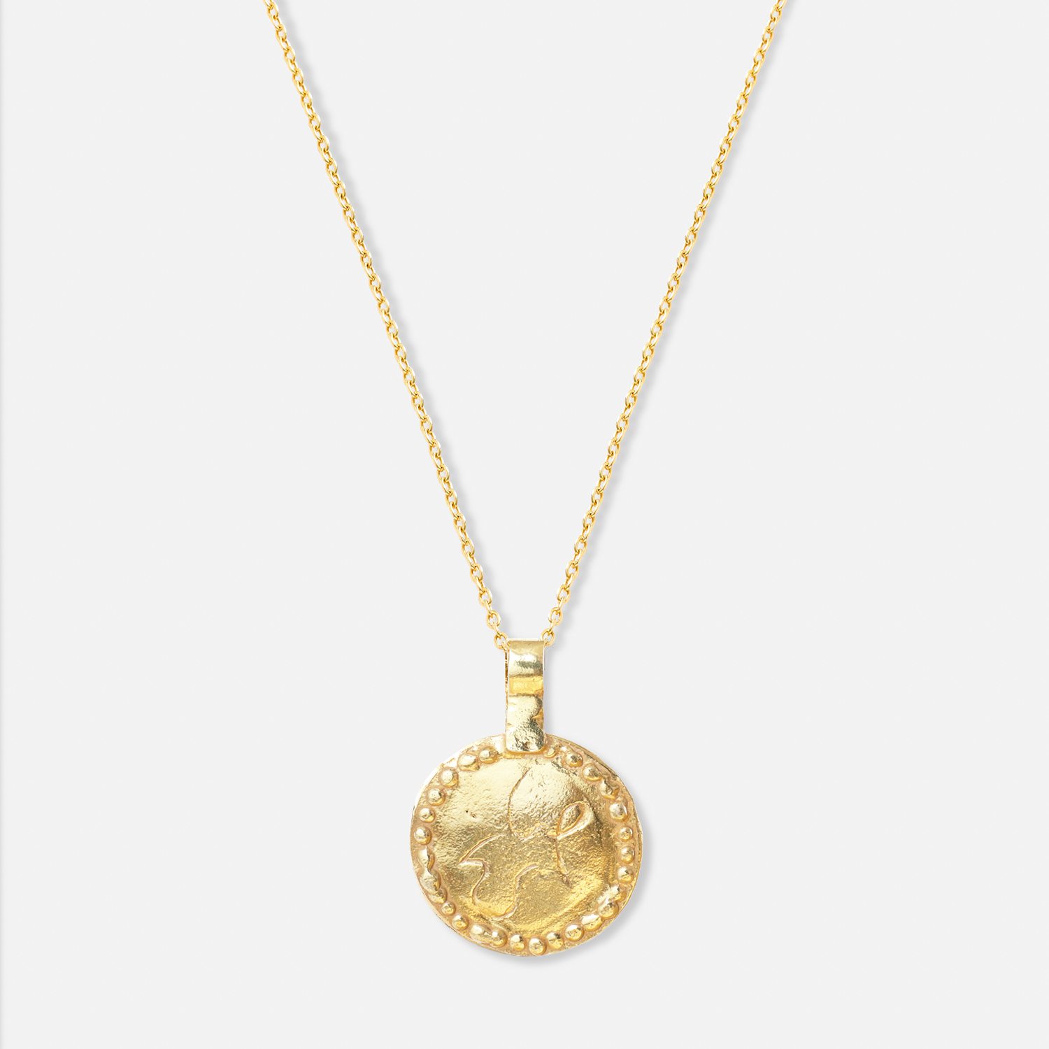 Back side of the gold-plated necklace with a circular pendant featuring a snow leopard and an emerald on one side, and the word "Peace" in Dari on this side.