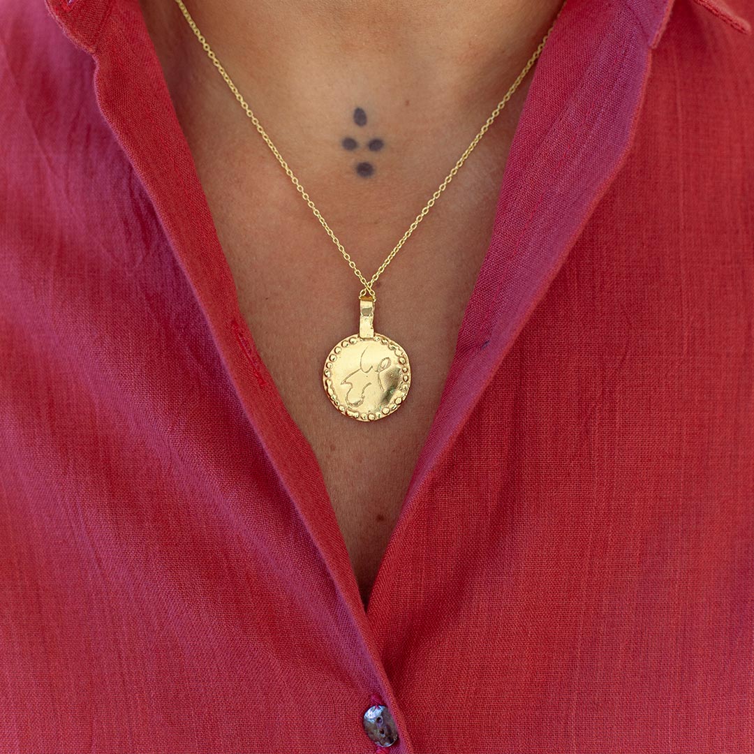 Gold-plated necklace with a pendant worn by a person in a raspberry shirt.