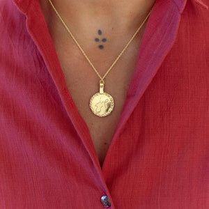 Gold-plated necklace with a pendant worn by a person in a raspberry shirt.