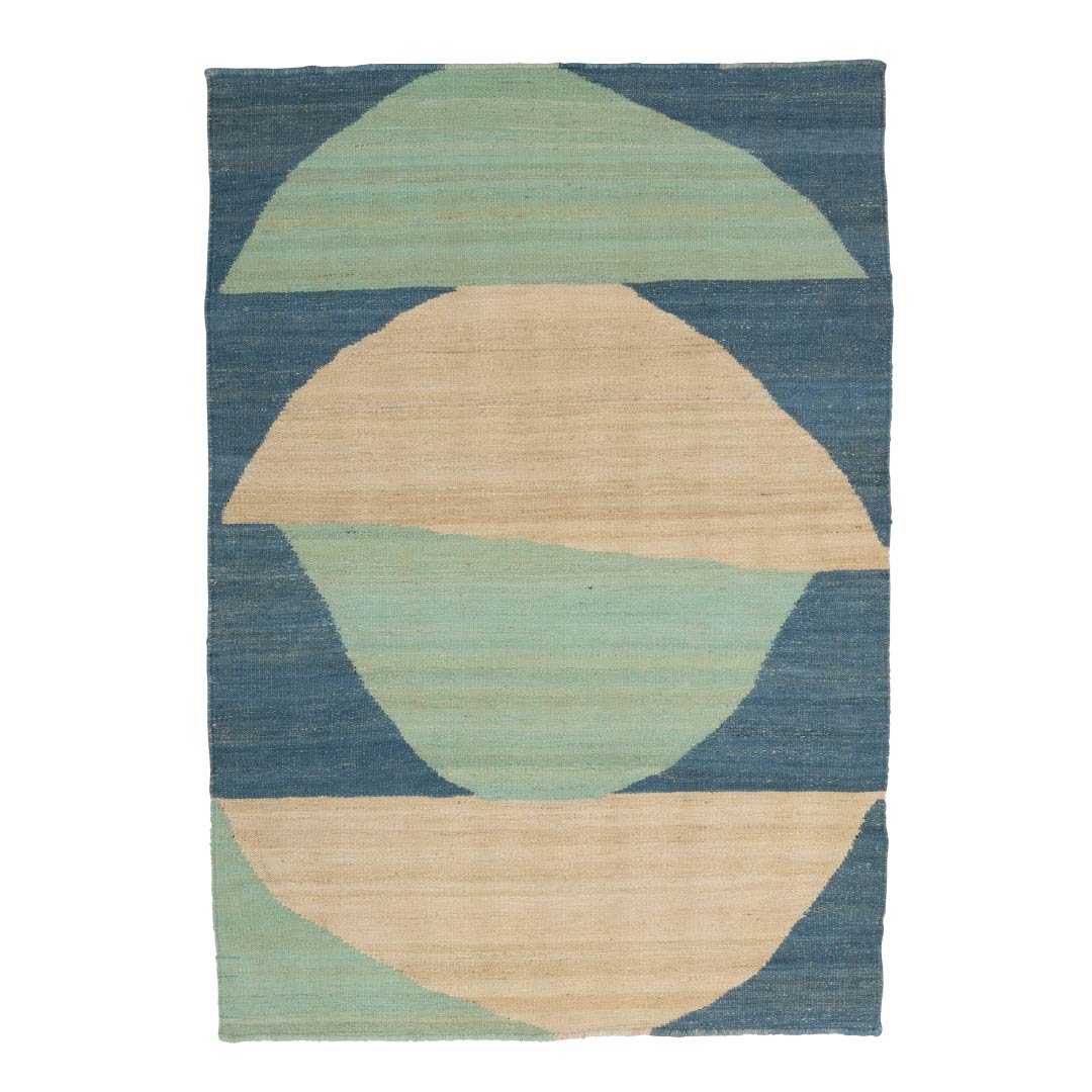 A rectangular area rug with a geometric abstract pattern featuring semi-circles in sage green and natural beige on a textured slate blue background.
