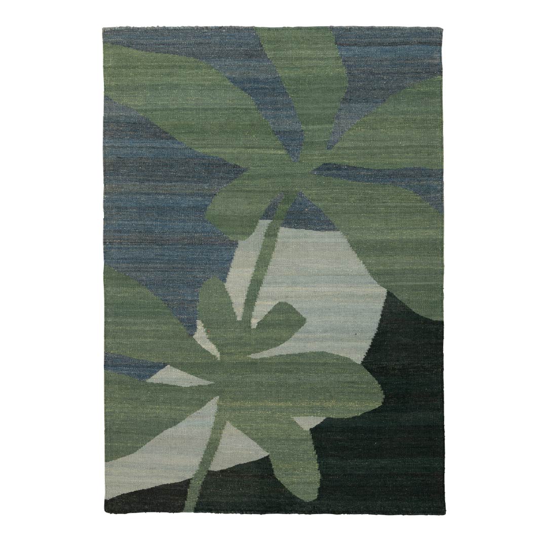 A rectangular area rug featuring a stylized tropical palm leaf pattern in shades of green, slate blue, and dark forest green, with a light beige geometric shape in the center.