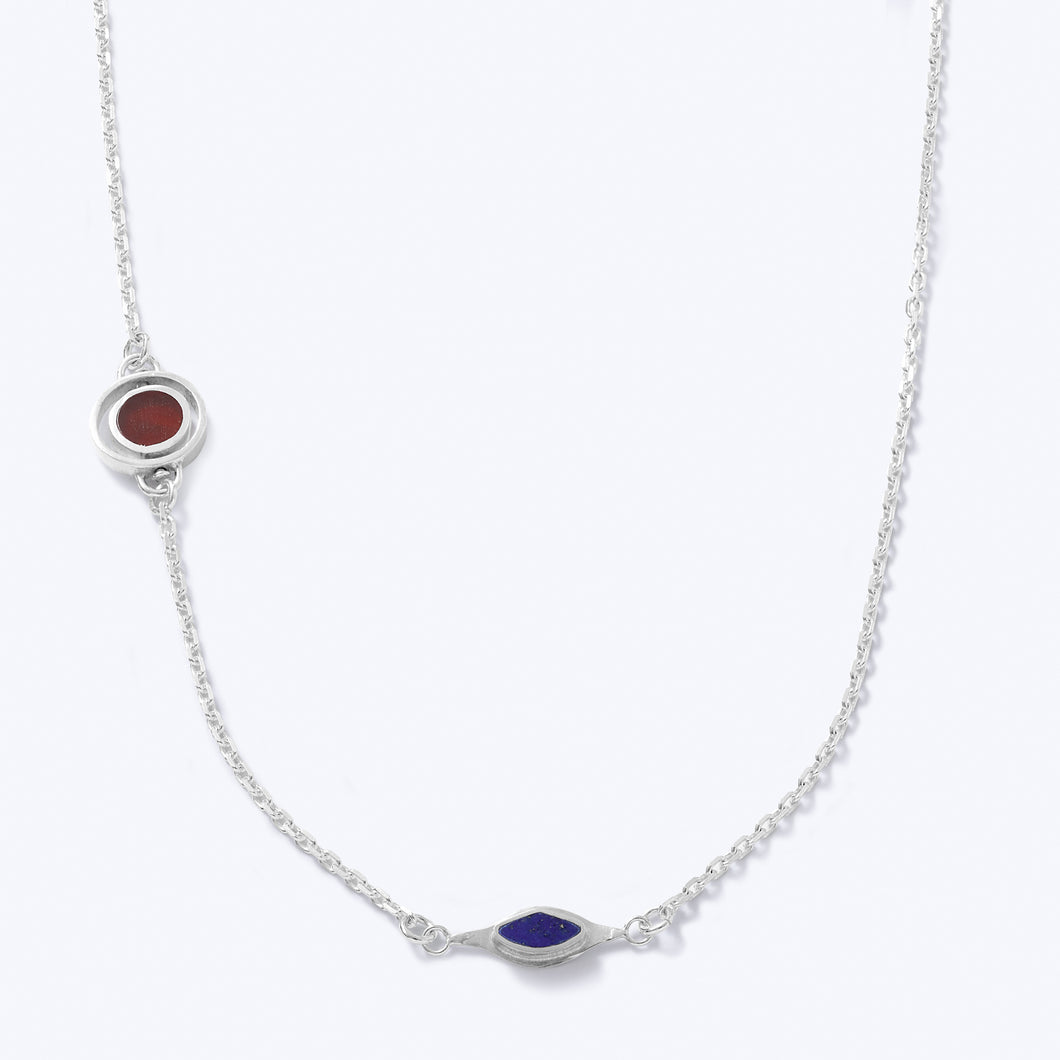 A sterling silver necklace with asymmetrical double charms, featuring Lapis and red Agate stones, displayed against a white background.