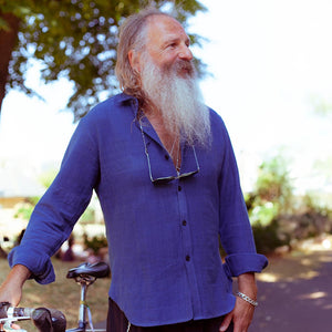 Man with a long white beard wearing a blue cotton shirt outdoors