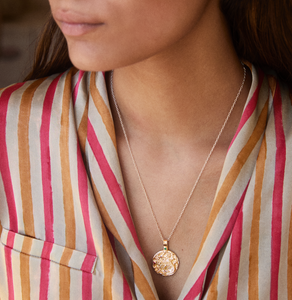 A gold-plated necklace with a circular pendant featuring a snow leopard and an emerald worn by a model in striped silk pyjamas.
